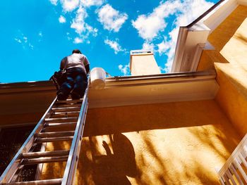 Low angle view of worker standing on ladder while repairing roof