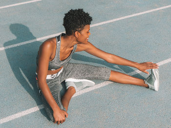 High angle view of smiling woman stretching leg on sports track
