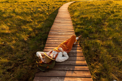 Woman naturalist resting lying on a backpack on wooden path through peat bog swamp in national park