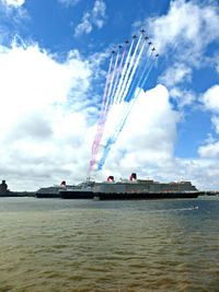 Low angle view of airshow by sea against sky