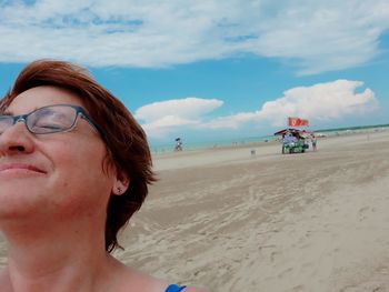 Close-up of woman smiling while standing at beach against sky