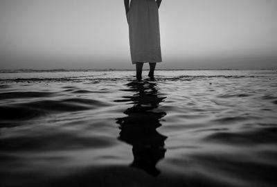 Low section of woman standing in sea against sky