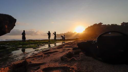 People at beach against sky during sunset