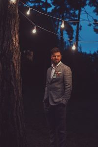 Portrait of young man standing by tree at night