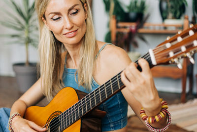 Close-up portrait of romantic blond young woman playing acoustic guitar sitting on the floor