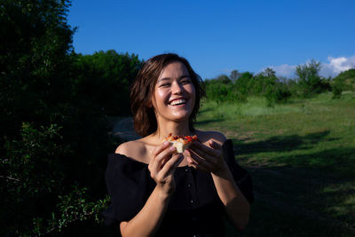 Smiling young woman eating food against plants