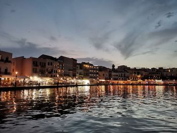 Buildings by illuminated city against sky at sunset