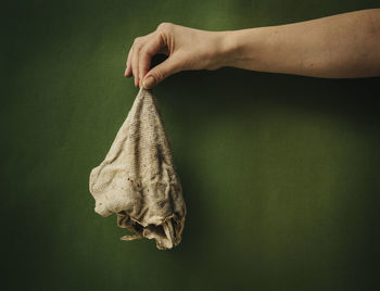 Close-up of human hand holding dirty fabric against green background