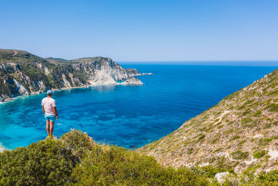 Rear view of man standing by sea against clear blue sky