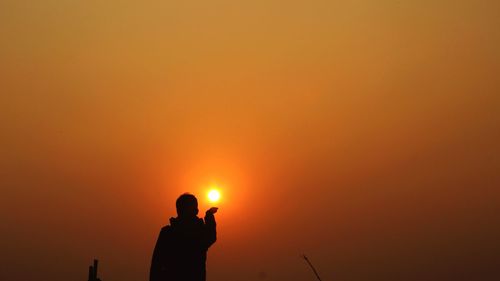 Silhouette man photographing orange sky during sunset