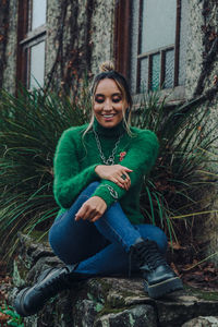 Portrait of smiling young woman using phone while sitting on tree