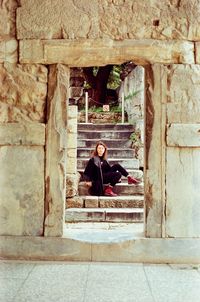 Full length of woman sitting on steps in old ruins