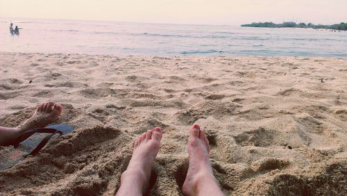 Low section of woman on sand at beach during sunset