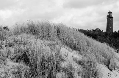 Scenic view of lighthouse next to grassy area against cloudy sky