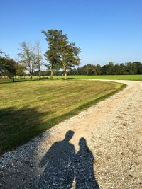 Shadow of people on dirt road against clear sky