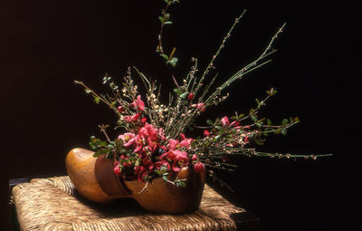 Close-up of flowers in wooden shoe on stool against black background
