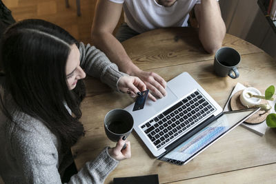 High angle view of couple having coffee and using credit card while shopping online through laptop at home