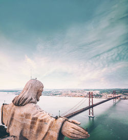 Statue of bridge over sea against cloudy sky