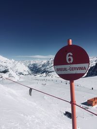 Information sign on snow covered landscape against clear blue sky