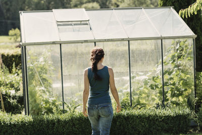 Rear view of female gardener walking against greenhouse