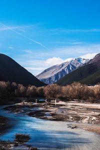 Scenic view of lake by snowcapped mountains against blue sky