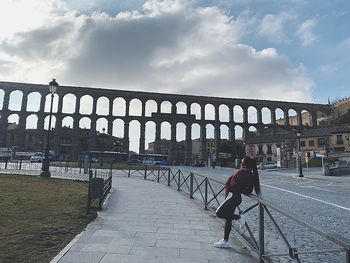 Rear view of woman on footpath by bridge against sky