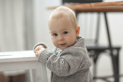 Portrait of a baby of 10 months in a knitted gray sweater, the concept of childhood and safety. 