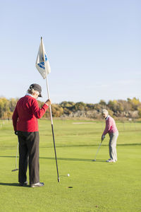 Senior woman putting while friend holding flag on golf course