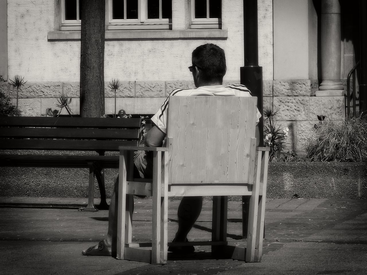 REAR VIEW OF MAN SITTING ON BENCH AGAINST BUILDING