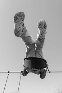 Low angle view of boy sitting on swing against clear sky