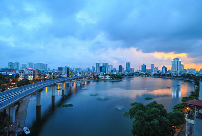 Illuminated buildings by river against sky in city