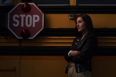 Young woman looking away while standing against bus at night