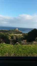 Scenic view of field by sea against sky