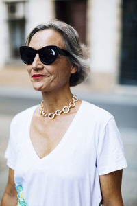 Happy woman in sunglasses standing on footpath