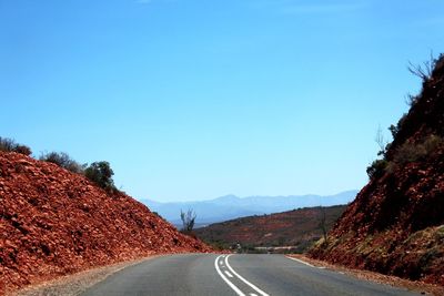 Road leading towards mountains against clear blue sky