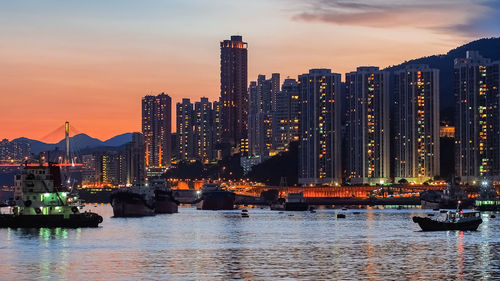 Sea by modern buildings against sky during sunset