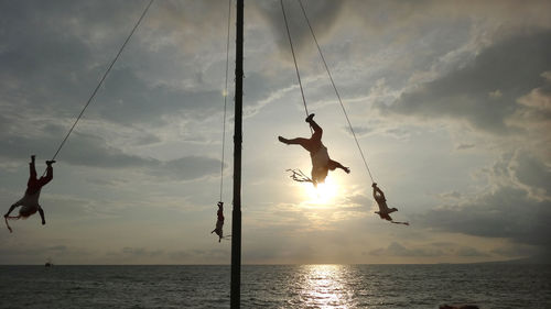 People hanging over sea against cloudy sky during sunset