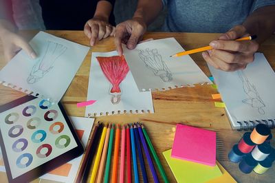 Cropped image of fashion designers sketching at desk in office