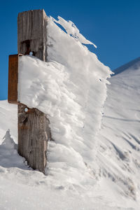 Frozen wooden post on snow covered field against sky