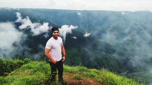 Portrait of smiling young man standing on mountain during foggy weather