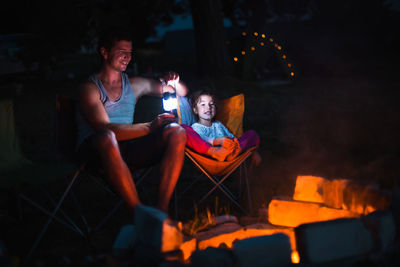 Father and daughter camping by bonfire at night