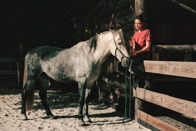 Full length of woman sitting by railing with horse