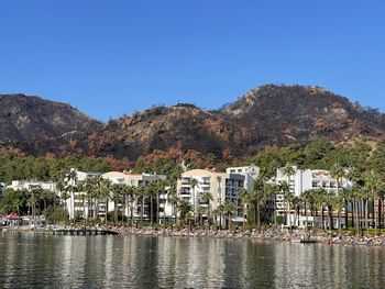 Buildings by lake against clear blue sky