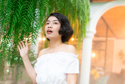 Woman looking away while standing against illuminated plants