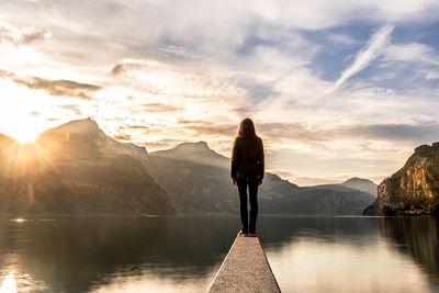 Rear view of woman standing by lake against sky