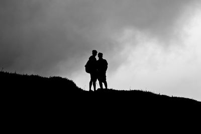 Silhouette of two men on the top of a hill