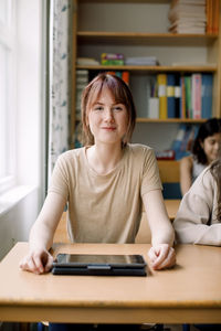 Smiling teenage girl with digital tablet on desk in classroom