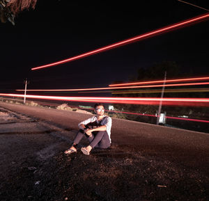 Man sitting by light trail on road at night