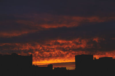 Low angle view of silhouette house against dramatic sky