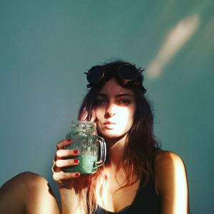 Portrait of young woman holding drink jar against wall